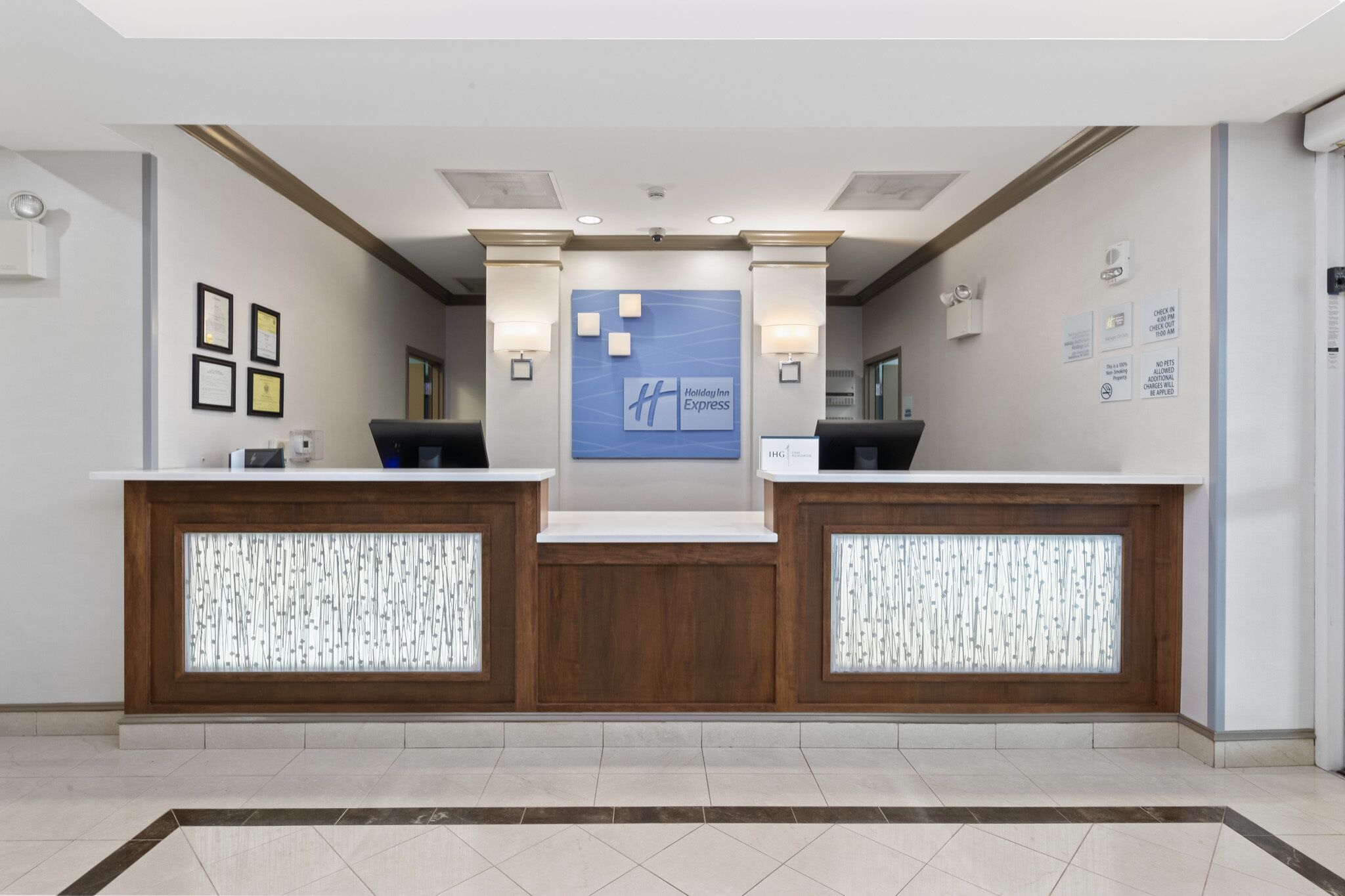 A reception area with two reception desks, a blue sign with 'Holiday Inn Express' logo, and framed certificates on the wall.