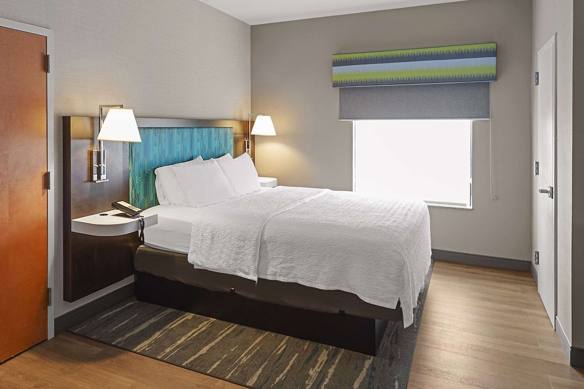 A hotel room with a bed, bedside tables, a window, and a painting on the wall.