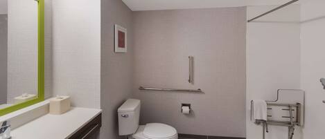 A modern bathroom with a toilet, sink, mirror, towel rack, and handrail.