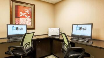 A hotel workspace with two desks, each with a computer and chair, a printer, and a framed artwork on the wall.
