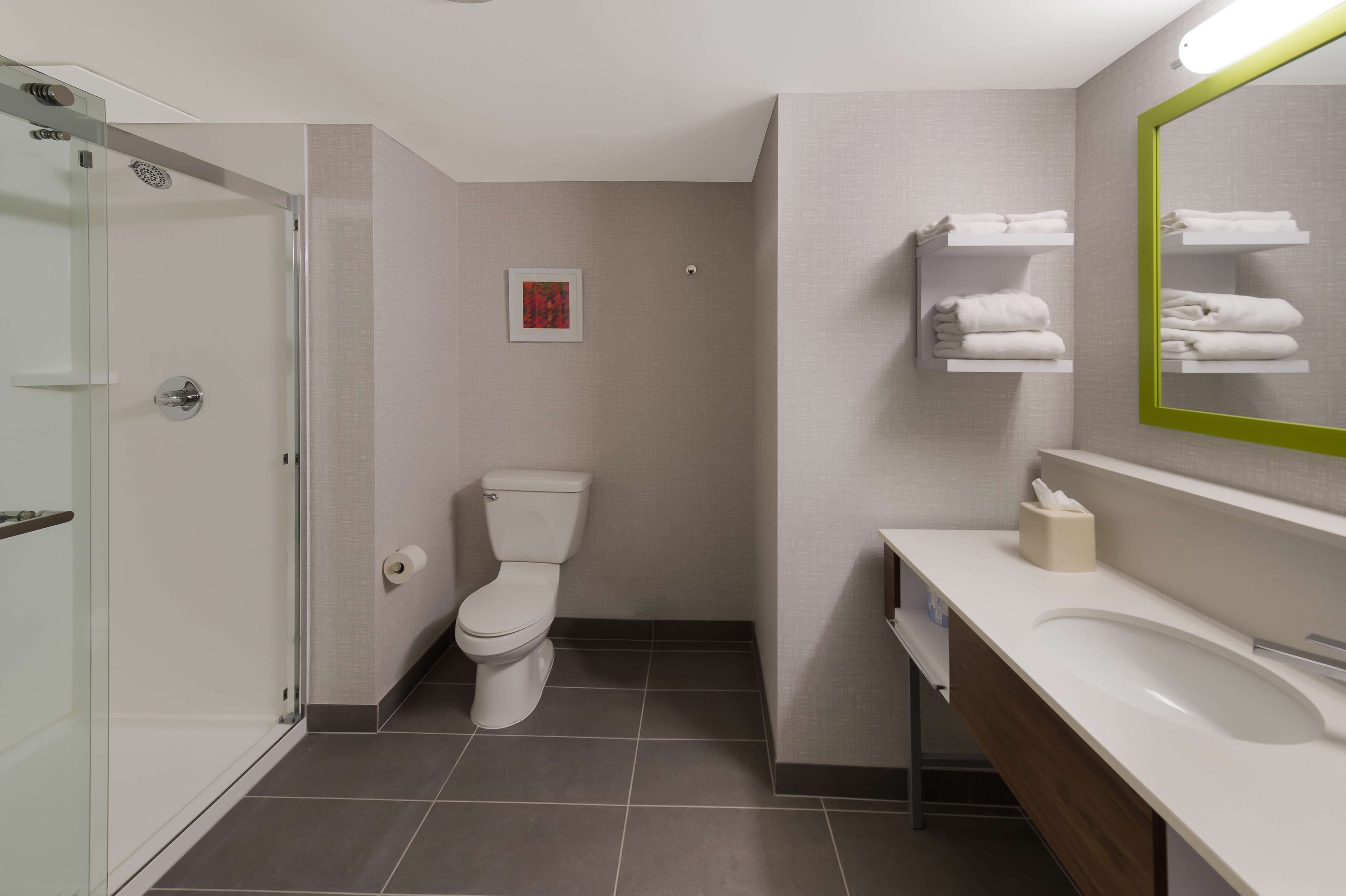 A modern bathroom with a glass shower enclosure, a toilet, a sink with a mirror, and towel racks.