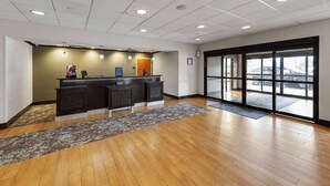 A hotel reception area with a wooden floor, a reception desk, and a large window with a view of the parking lot.