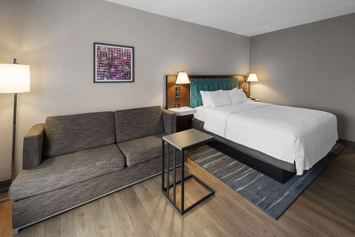 A hotel room with a bed, a sofa, a small table, and two bedside lamps.