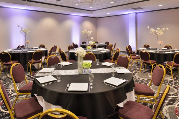 Un salón de conferencias con mesas redondas, sillas y centros de mesa con flores.