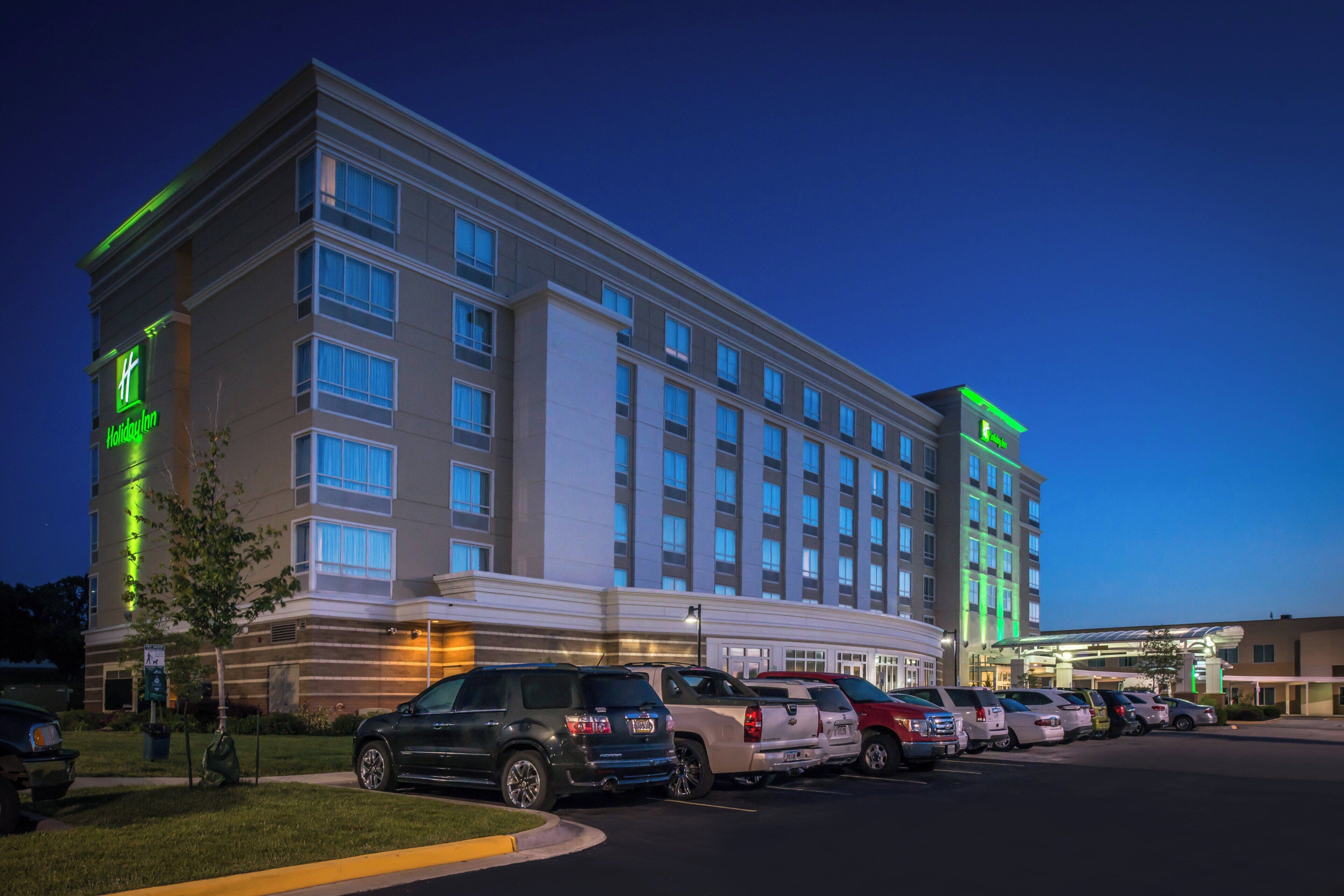 A multi-story hotel with a row of parked vehicles in front.
