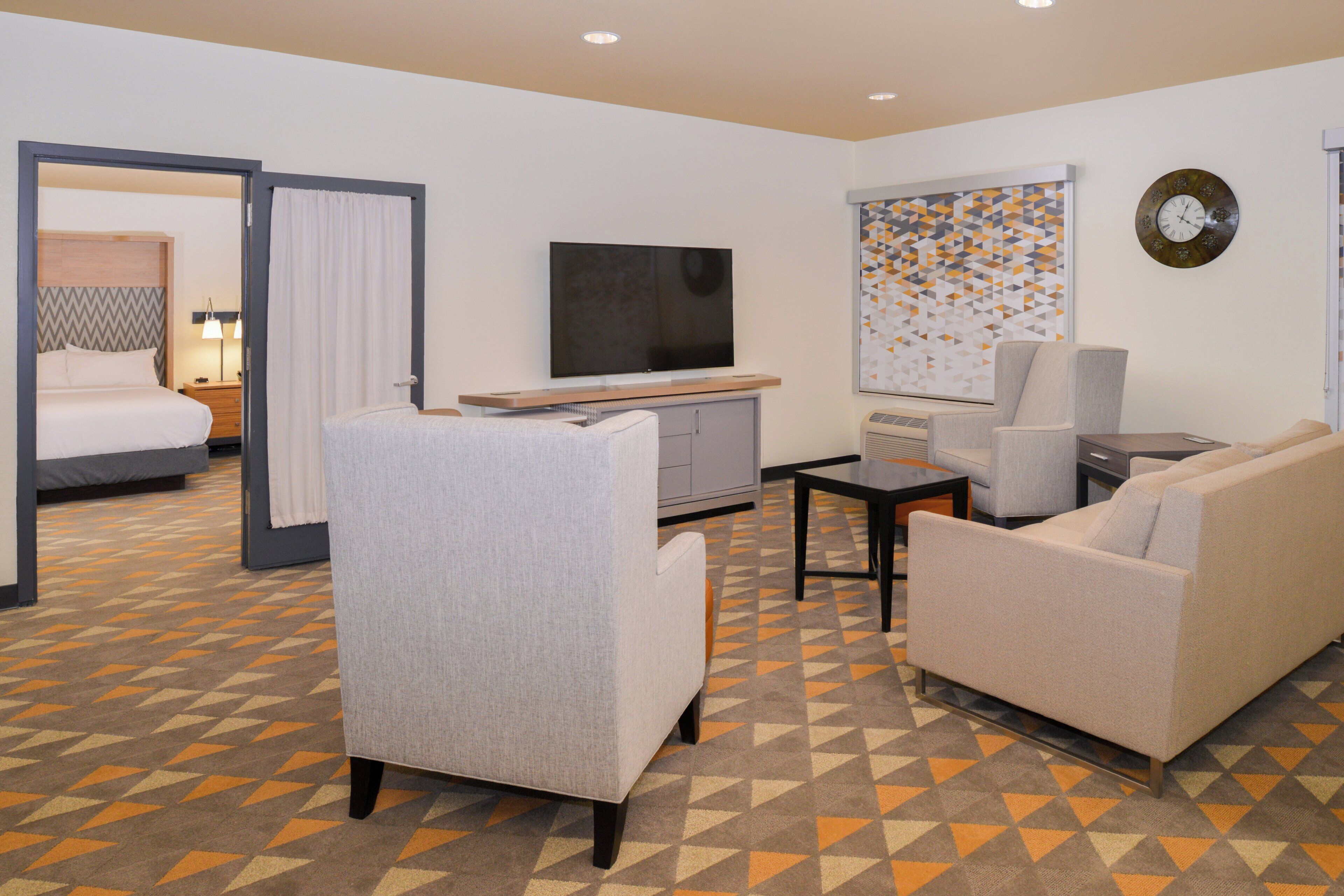 A hotel room with a bed, a TV, a sofa, a chair, and a carpet with a geometric pattern.