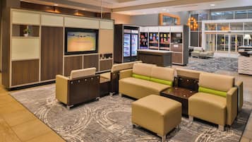 Un espace de détente moderne comprenant un ensemble de canapés, un téléviseur, un réfrigérateur rempli de boissons et une machine à café.