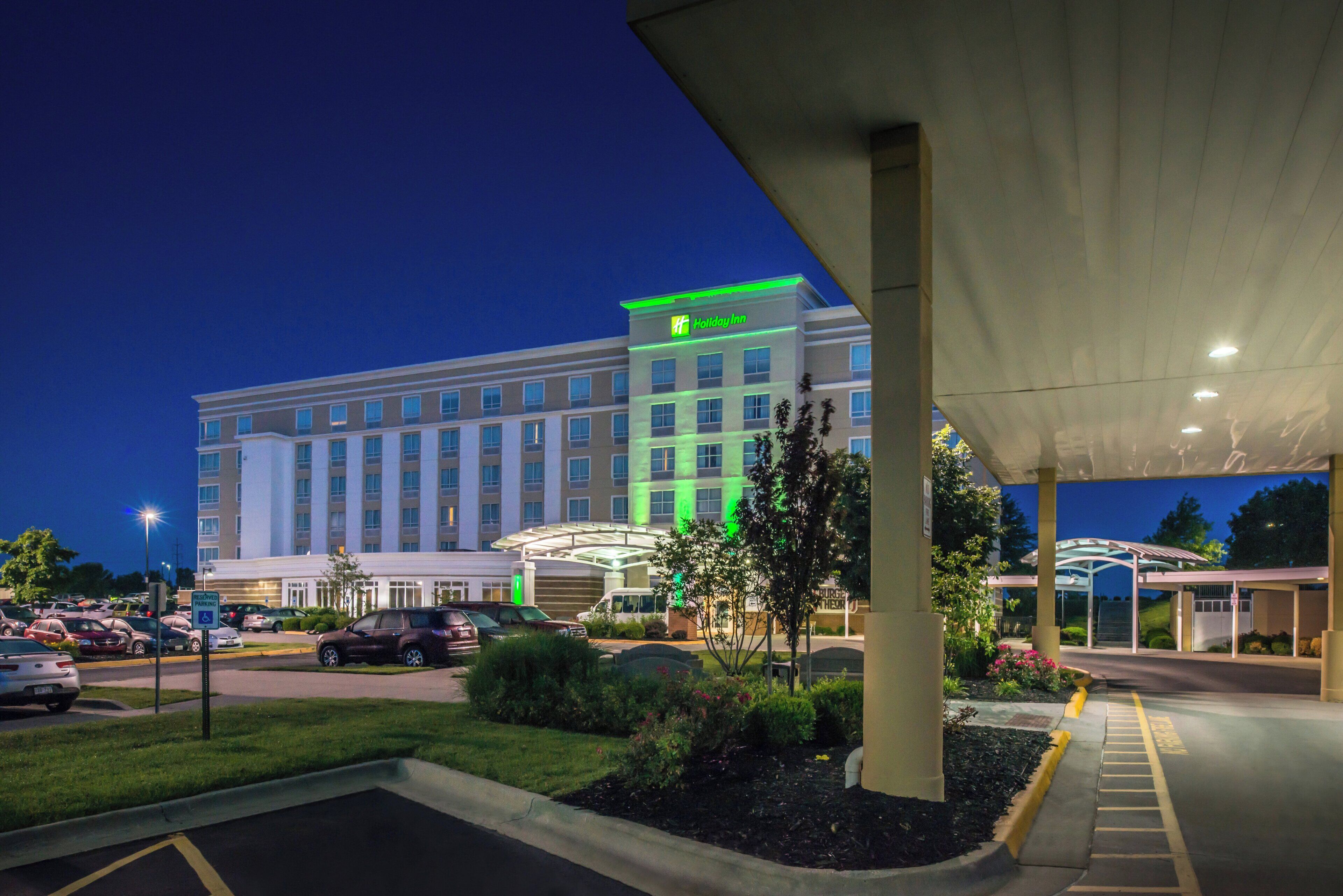 Un hotel con un amplio estacionamiento, un corredor cubierto y un edificio con señalización iluminada.