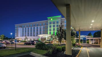Un hotel con un amplio estacionamiento, un corredor cubierto y un edificio con señalización iluminada.