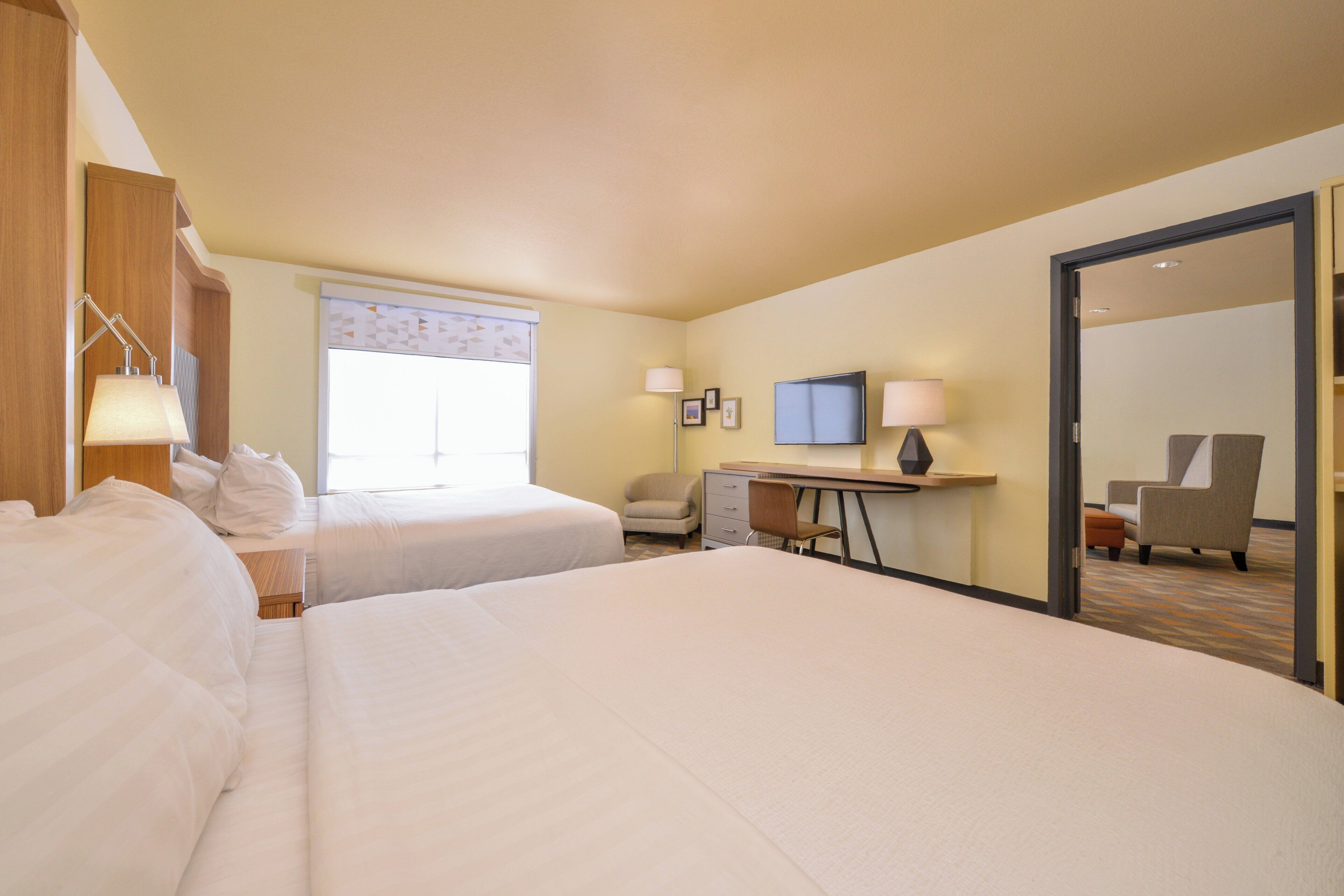 Habitación de hotel con dos camas, un escritorio, una silla, un televisor y una puerta que da a otra habitación.