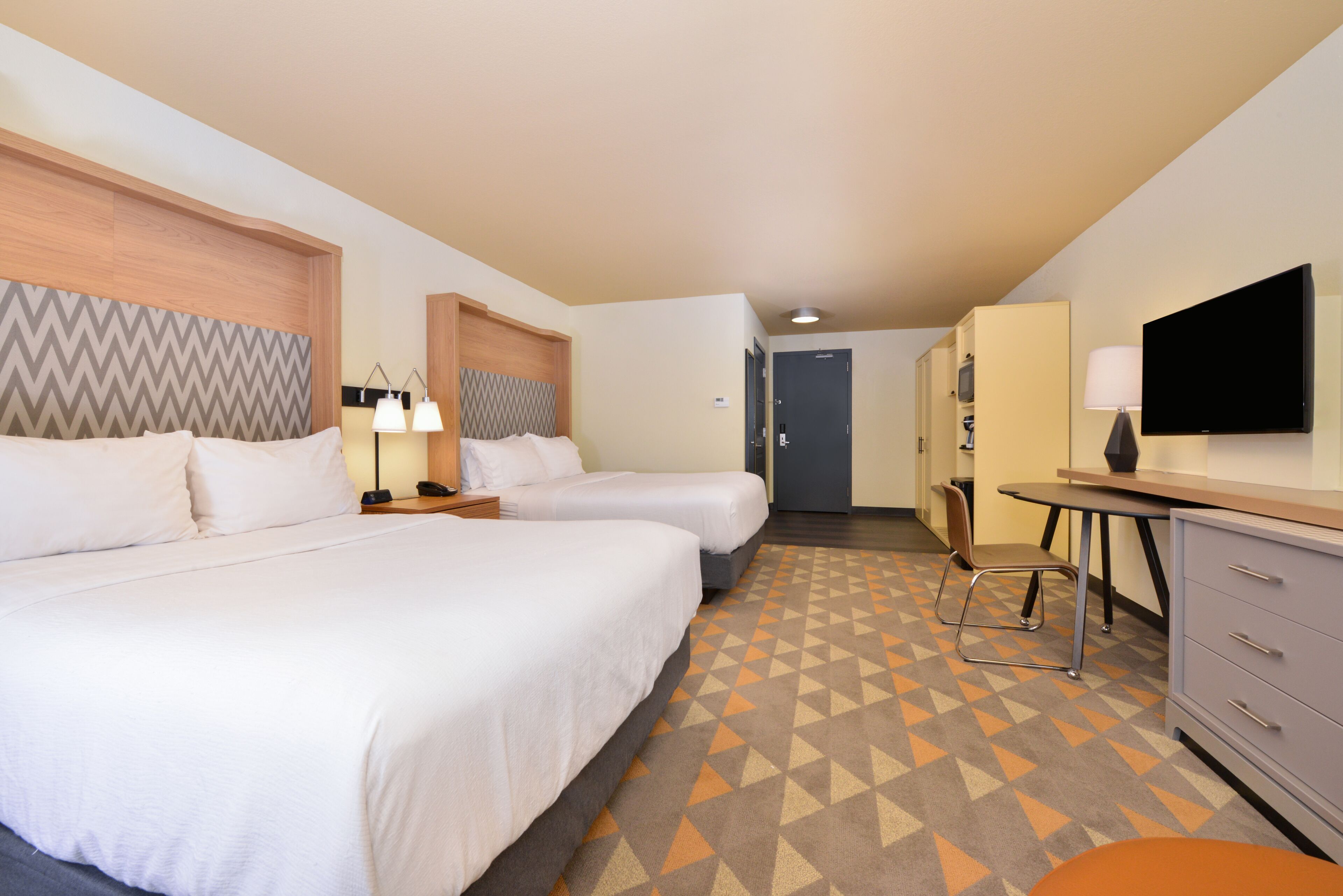 A hotel room with two beds, a desk, a chair, a TV, and a wardrobe.
