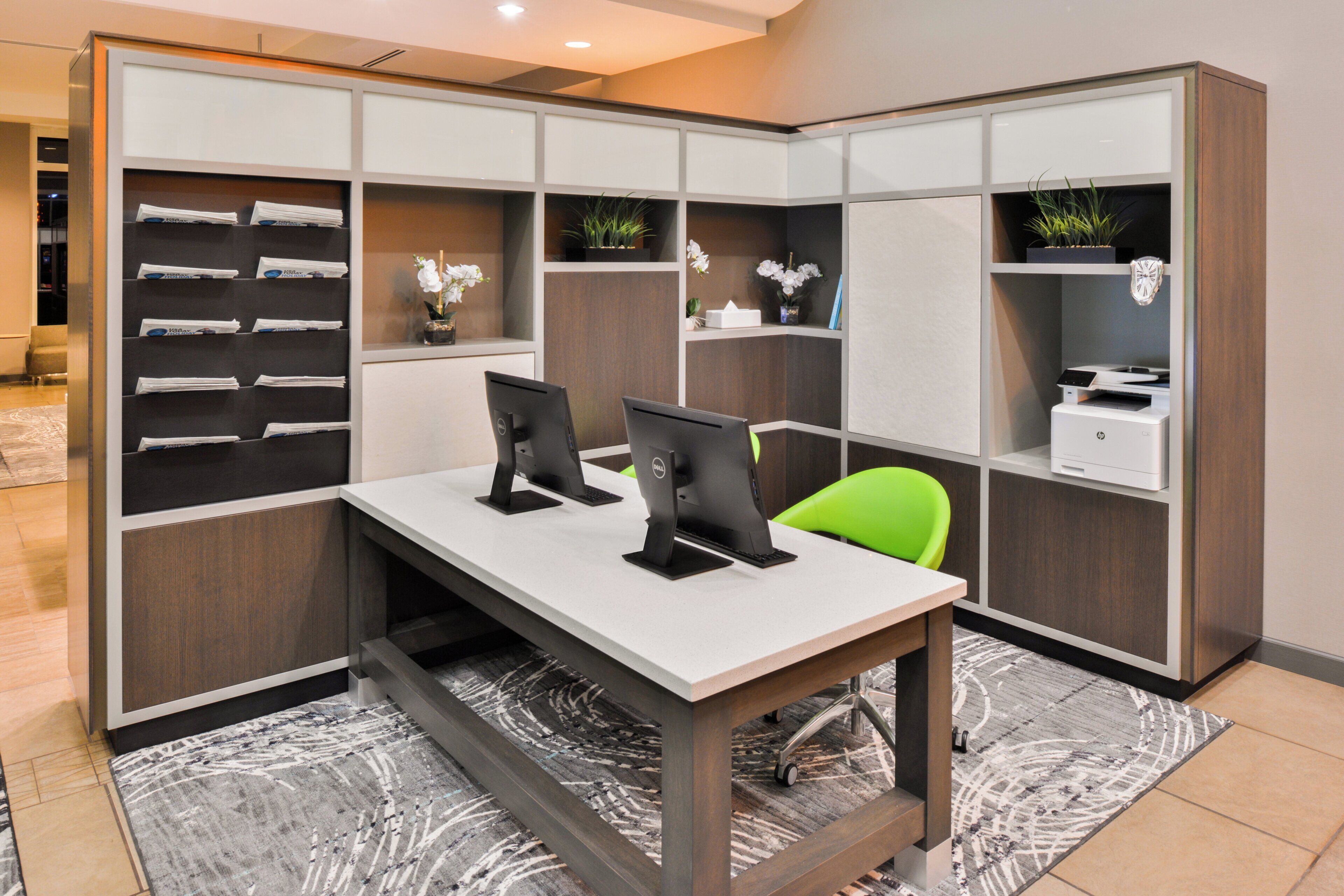Un espace de bureau moderne comprenant un bureau, deux écrans d’ordinateur, une chaise verte et un classeur contenant des documents.