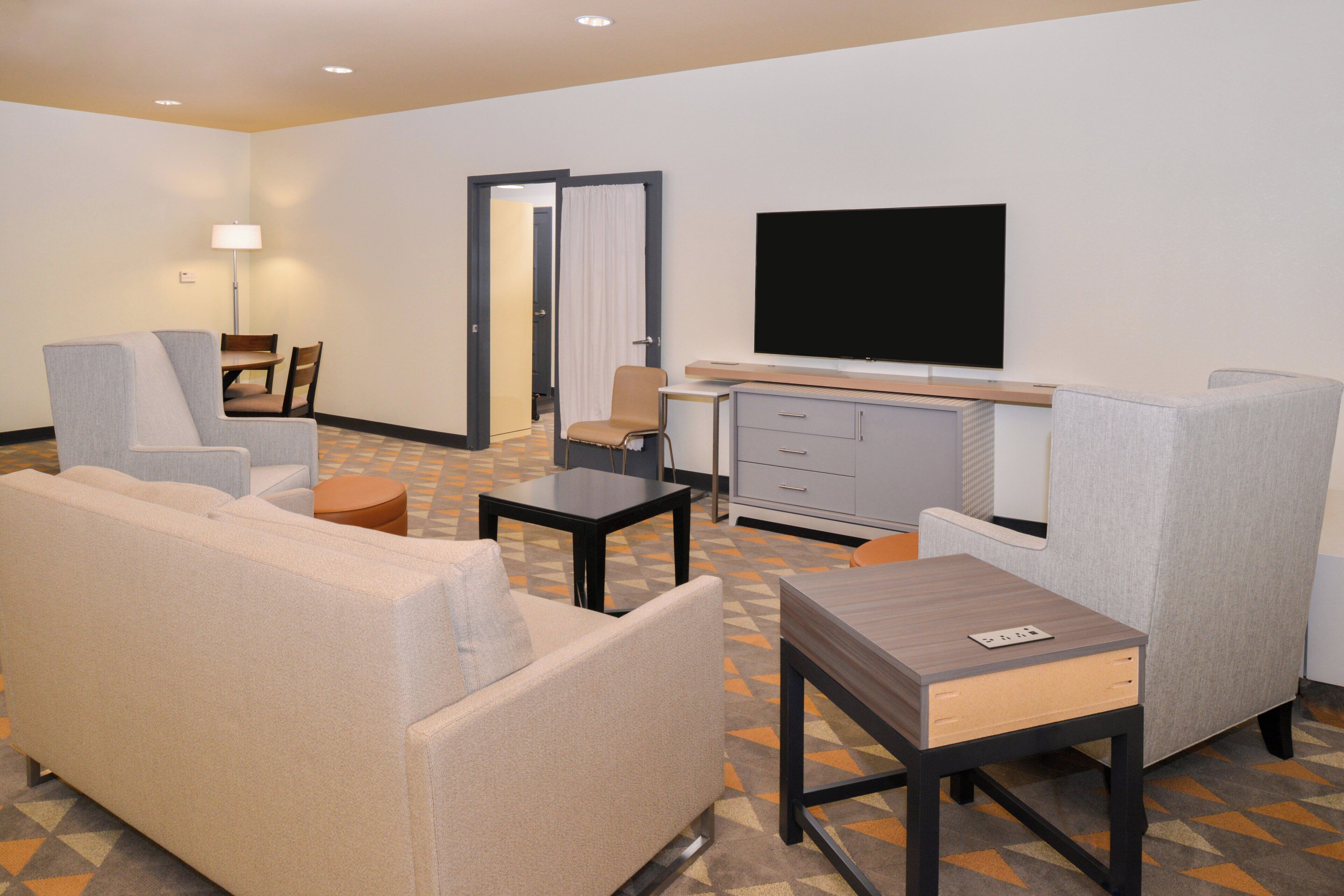 Una habitación de hotel con sofá, sillón, una mesita, televisor y armario.