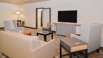Una habitación de hotel con sofá, sillón, una mesita, televisor y armario.