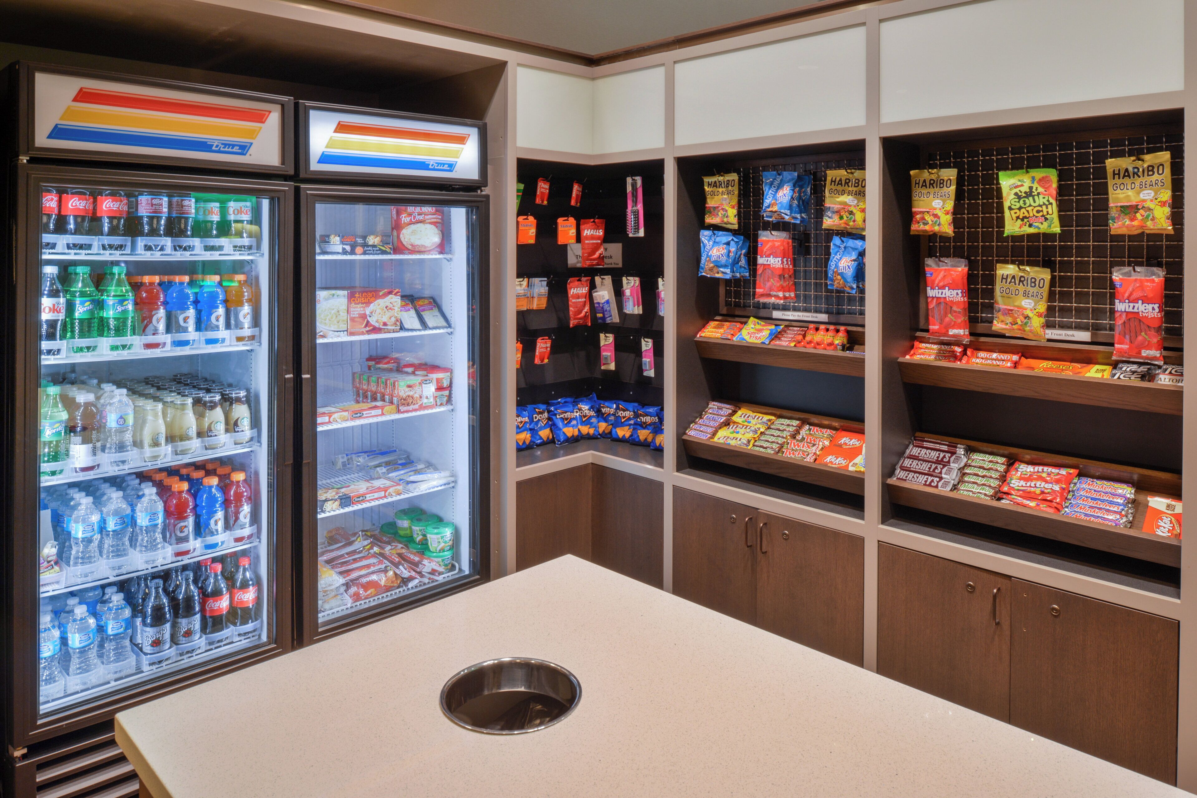 Ein Getränkeautomat mit verschiedenen Getränken und Snacks, ein Kühlschrank mit Getränken sowie Regale voller Snacks und Süßigkeiten.