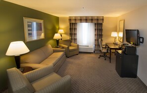 Quarto de hotel com sofá, poltrona, escrivaninha, televisão e duas luminárias.