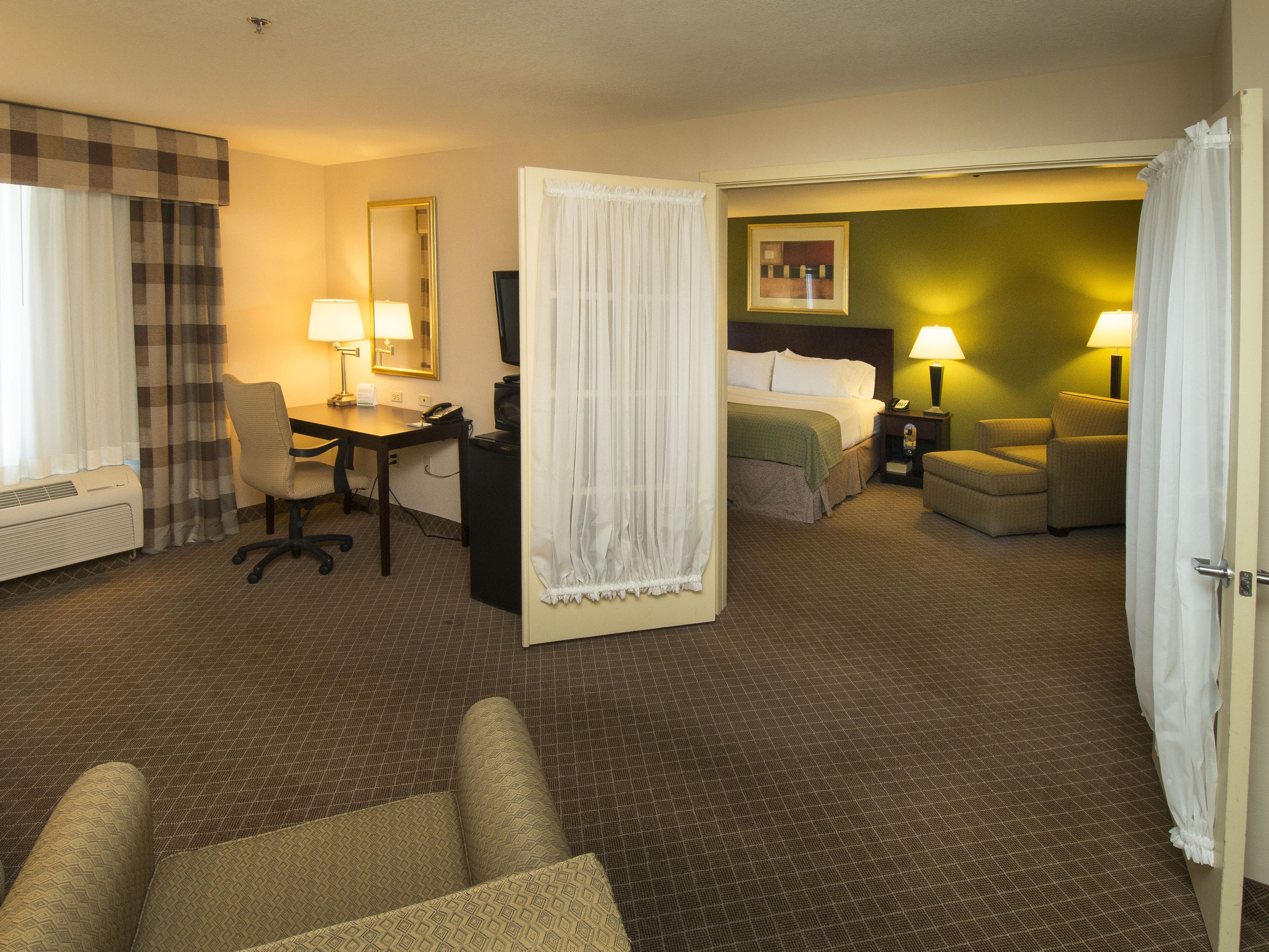 A hotel room with a desk, two chairs, a bed, and a television.