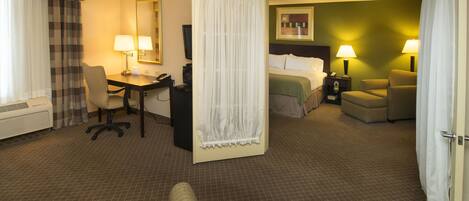 A hotel room with a desk, two chairs, a bed, and a television.