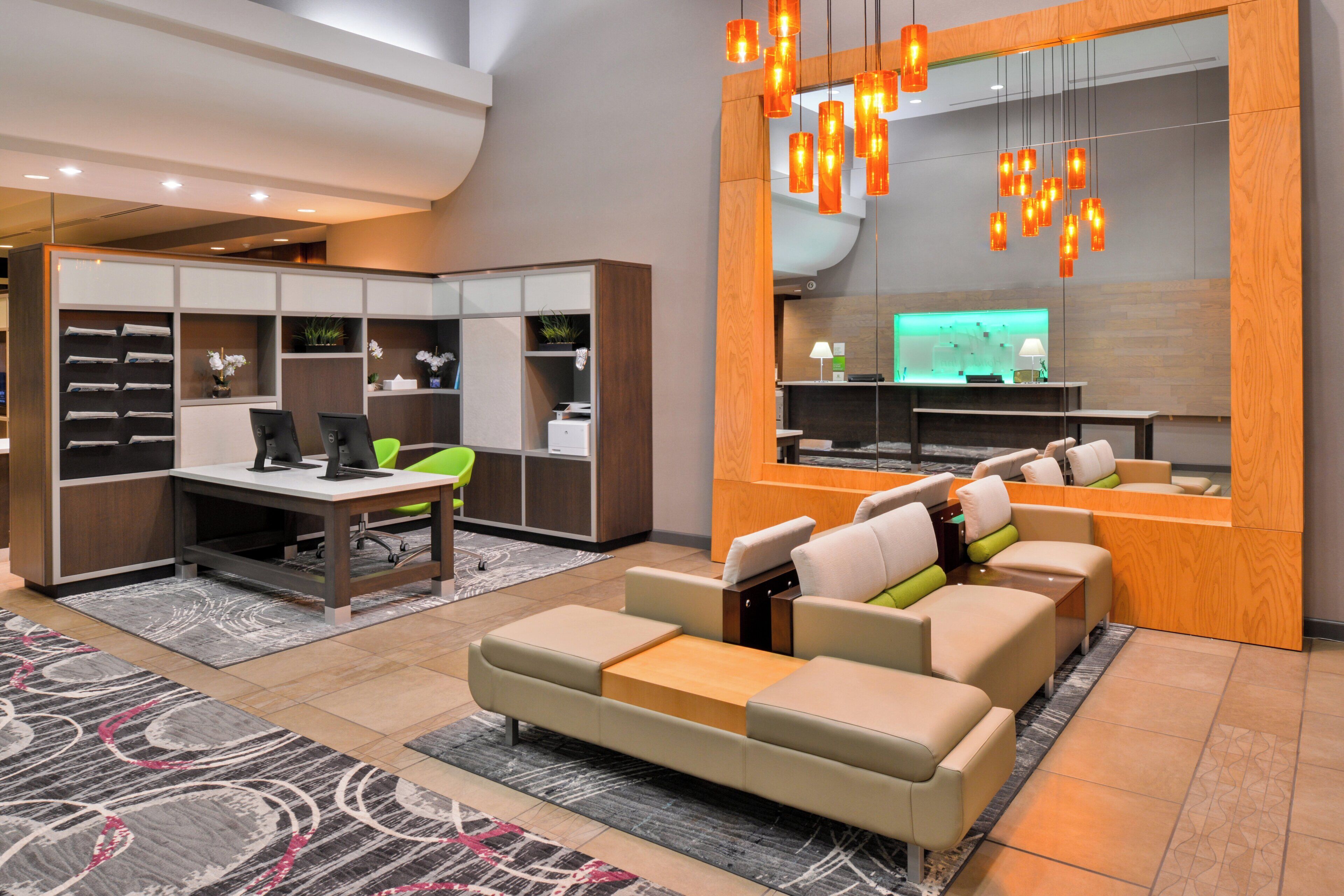Un vestíbulo de hotel moderno con recepción, zona de estar y un espejo grande.