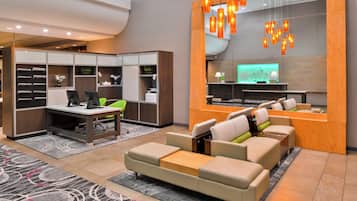 Un vestíbulo de hotel moderno con recepción, zona de estar y un espejo grande.