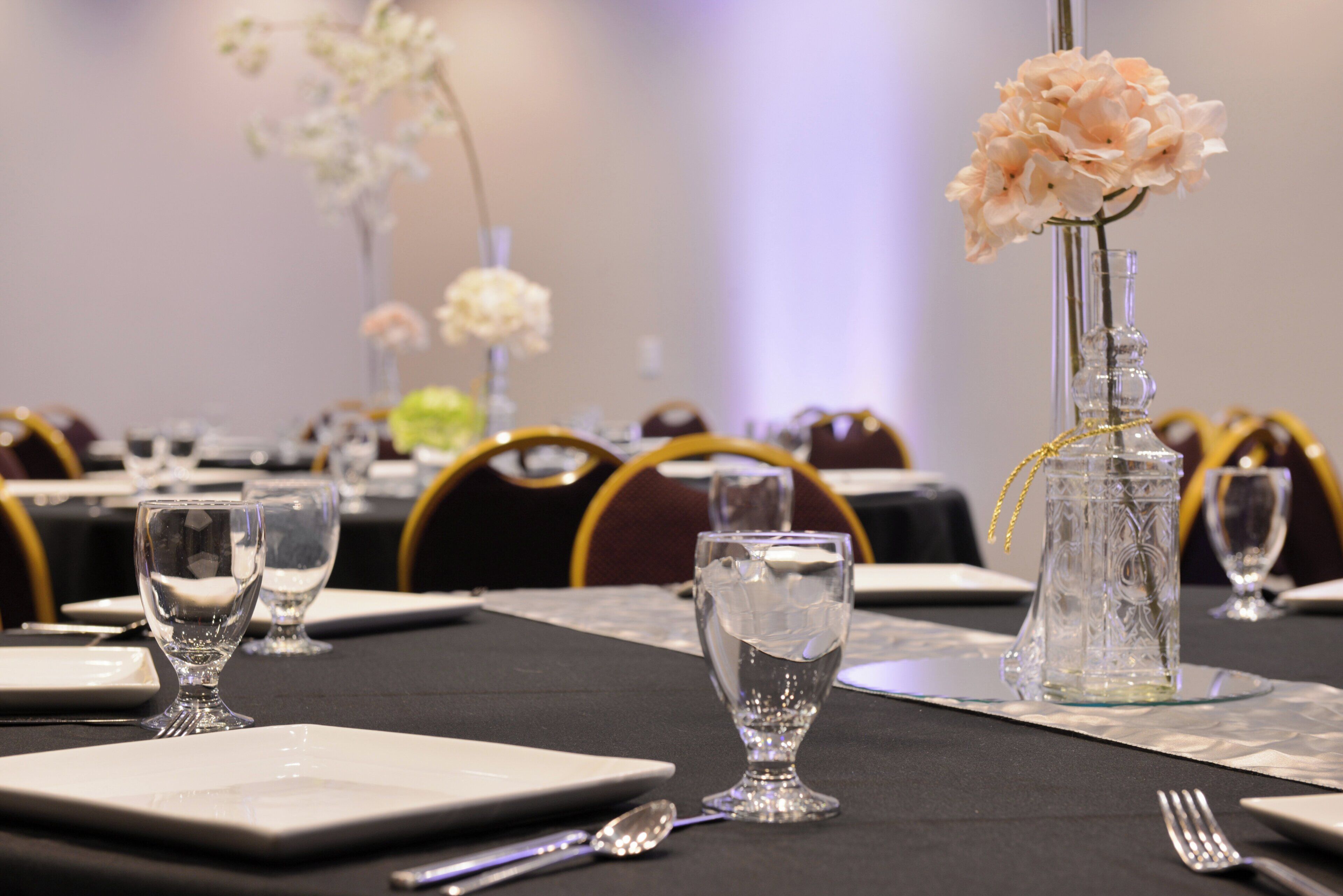 A table set for a formal event with clear glassware, a vase with flowers, and a decorative glass bottle.