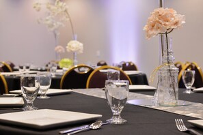 A table set for a formal event with clear glassware, a vase with flowers, and a decorative glass bottle.