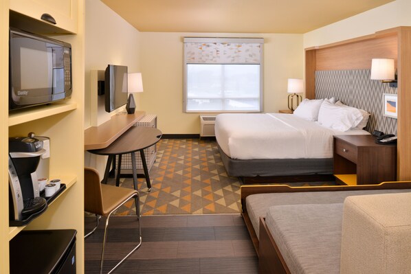 Quarto de hotel com uma cama, uma mesa com cadeira, televisão, máquina de café e janela com persianas.