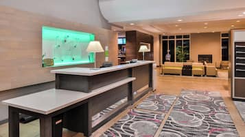 Um saguão de hotel com balcão de recepção, área de bar e espaço de estar com sofás.