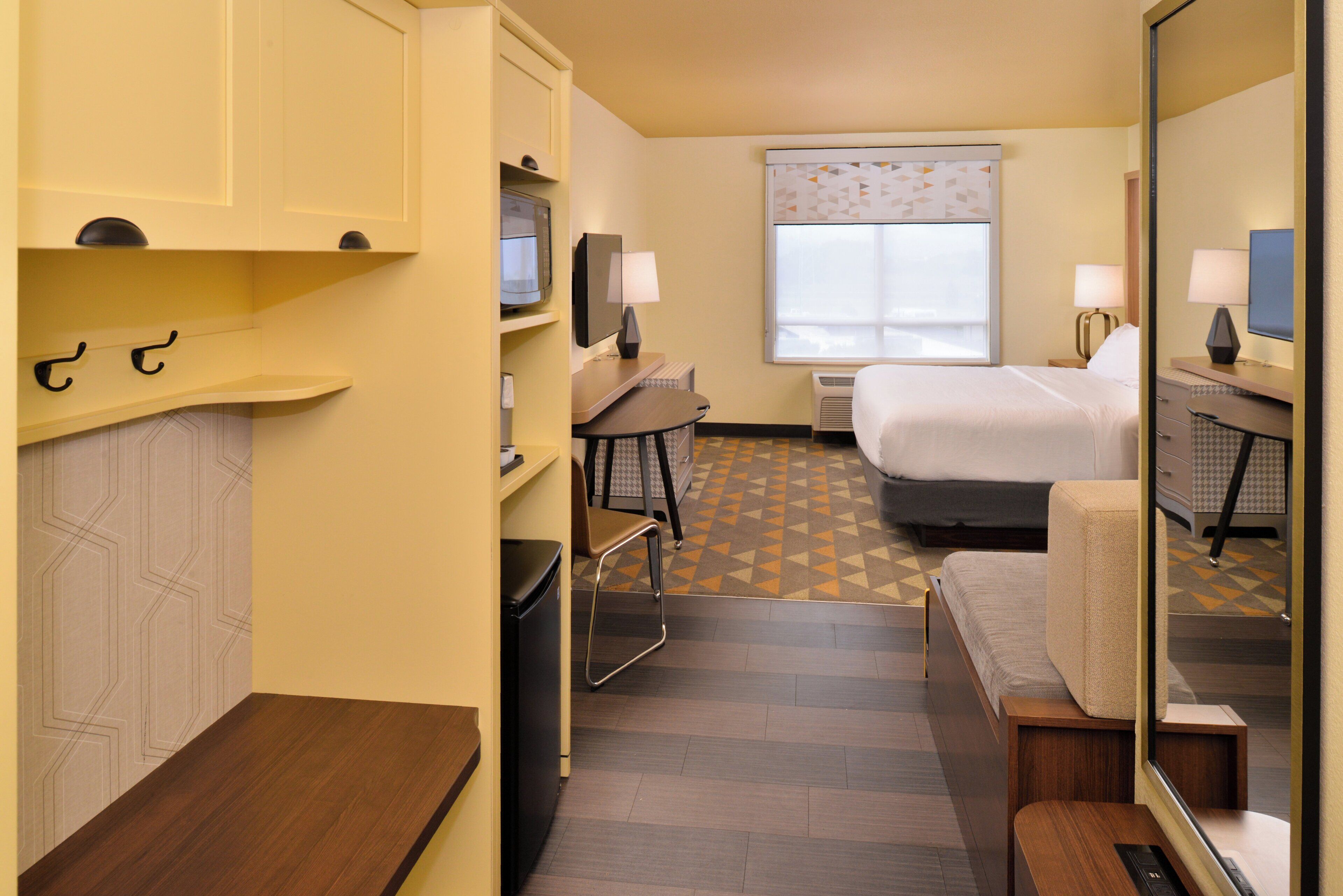 A hotel room with a bed, a desk, a chair, a television, a window, and a mirror.