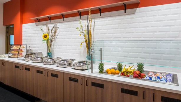 Un mostrador de buffet con diversos alimentos, entre ellos frutas y pasteles, y una vitrina de vidrio.