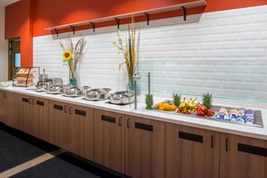 Un comptoir de buffet proposant une variété de plats, notamment des fruits et des pâtisseries, ainsi qu’une vitrine réfrigérée.