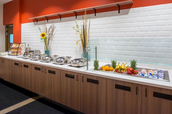 Un mostrador de buffet con diversos alimentos, entre ellos frutas y pasteles, y una vitrina de vidrio.