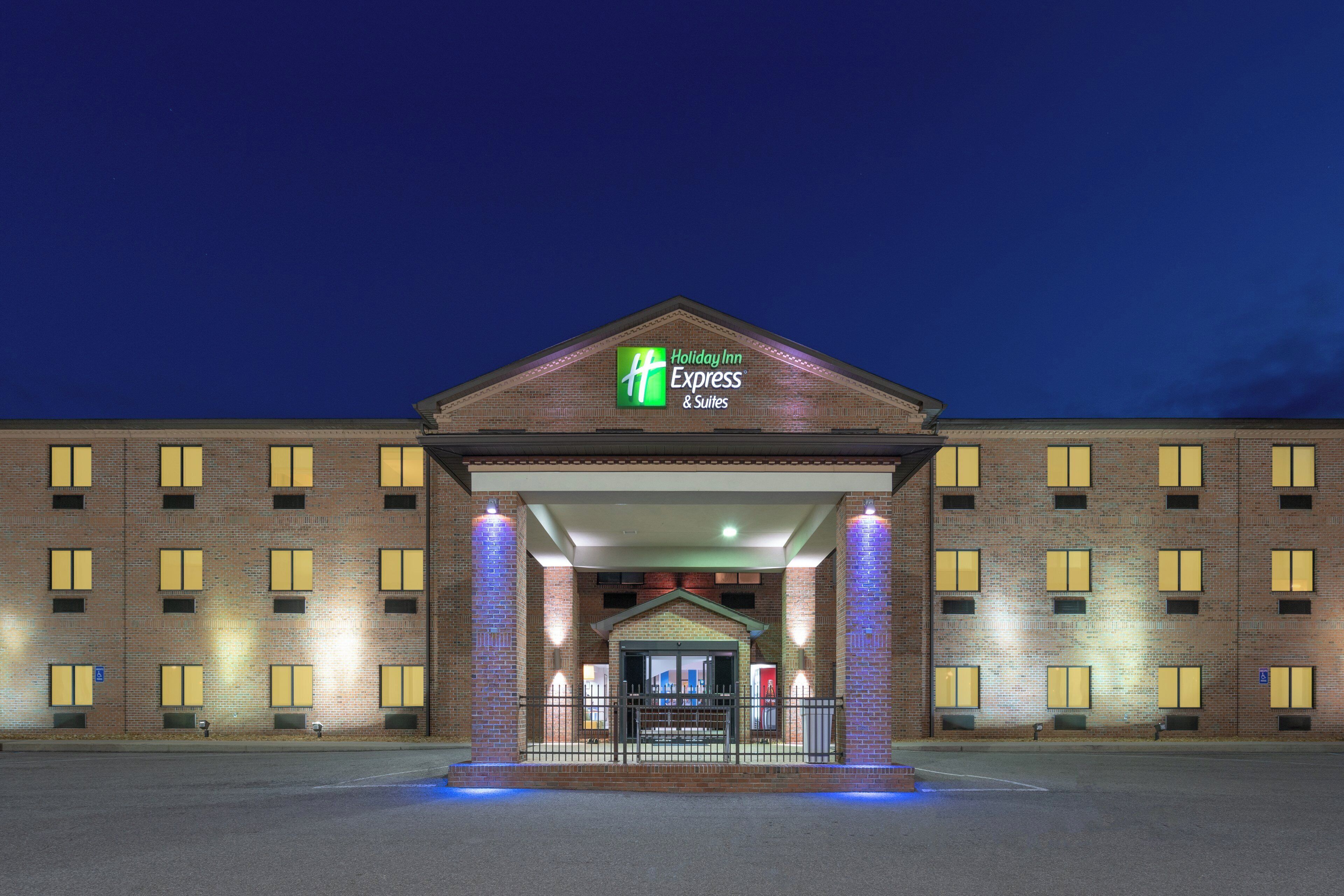 Un bâtiment de la chaîne Holiday Inn Express & Suites, avec une façade en briques, de nombreuses fenêtres et une entrée bien éclairée.