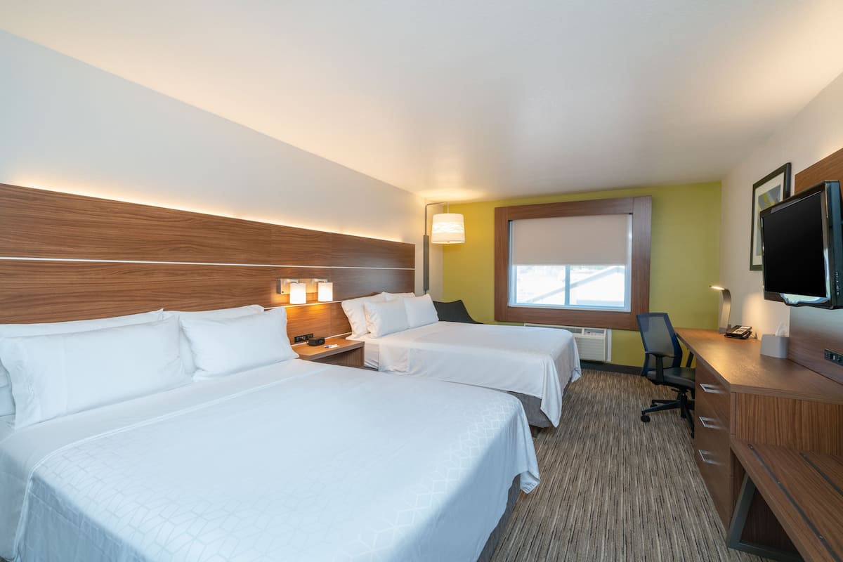 A hotel room with two beds, a desk, a chair, a TV, and a window.