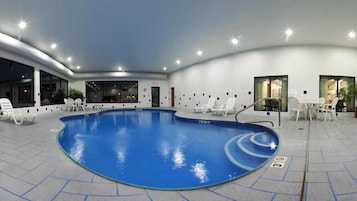 Una piscina interior de diseño curvo, rodeada de sillas reclinables blancas y un piso de baldosas.