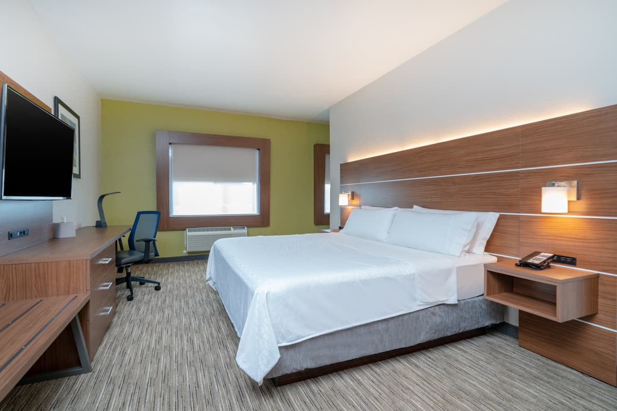 A hotel room with a bed, desk, chair, and a TV.