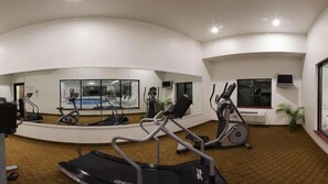 Une salle de sport équipée de tapis de course, d’un vélo d’appartement et d’un mur miroir qui reflète l’équipement.