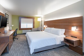 Une chambre d’hôtel avec un grand lit, un bureau avec un ordinateur, une chaise, une télévision et une fenêtre avec des stores.