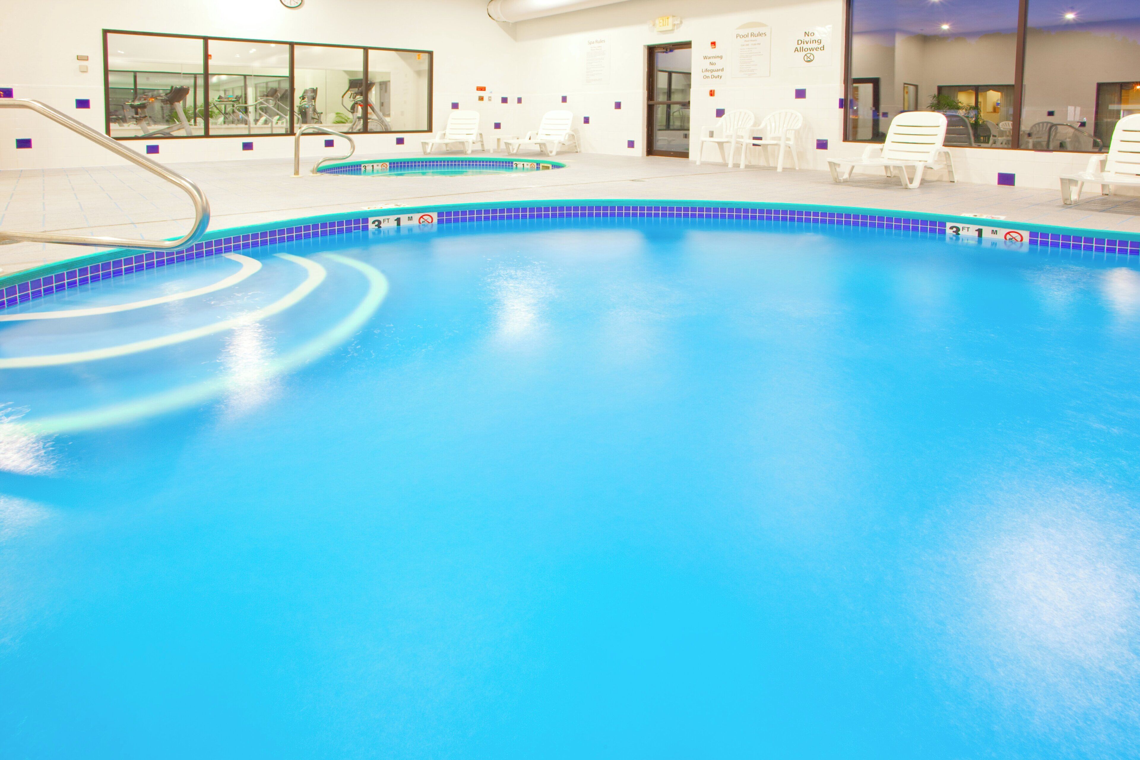 Una piscina interior con agua cristalina, un trampolín y sillas de descanso alrededor del borde.