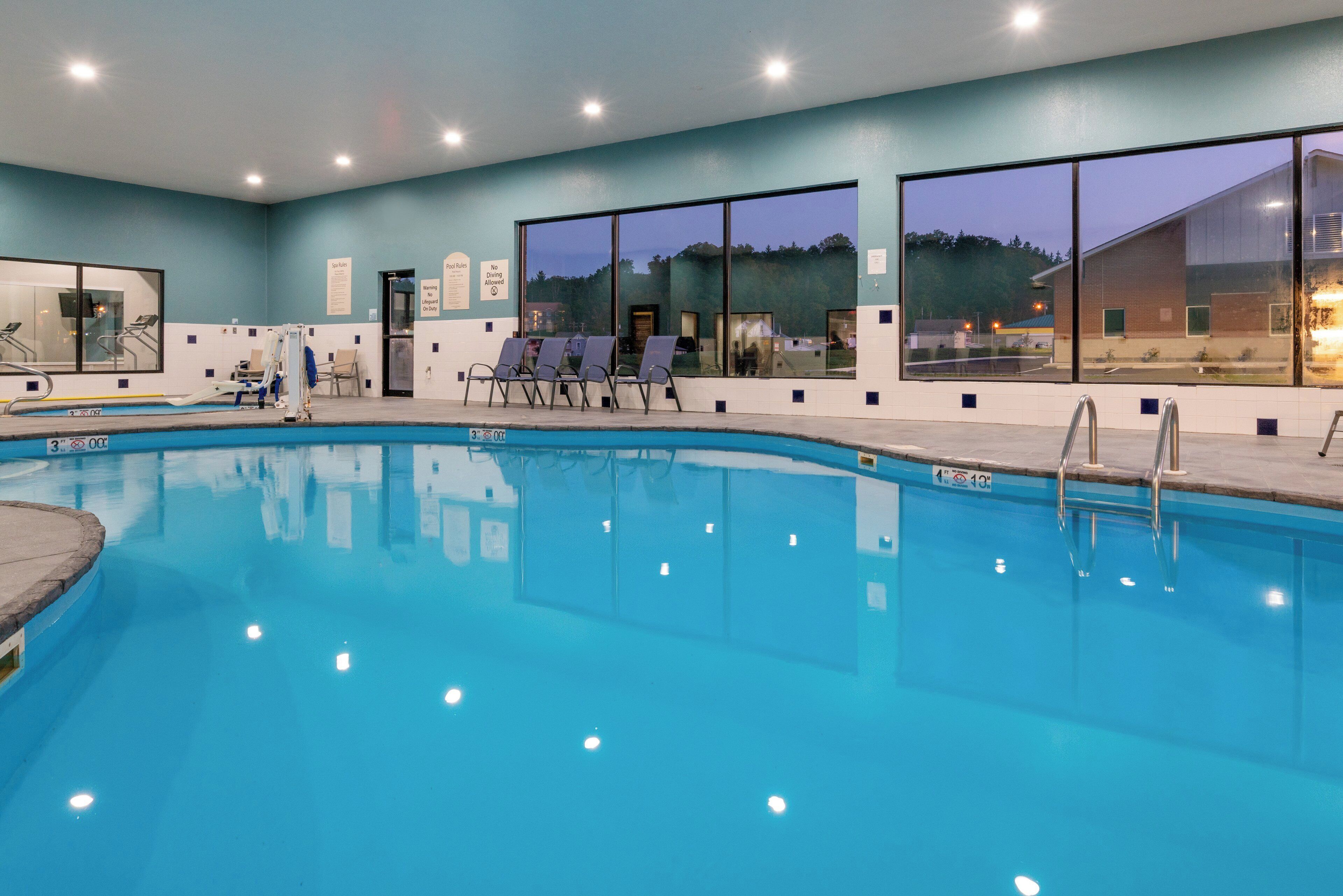 An indoor swimming pool with clear water, a diving board, and lounge chairs.