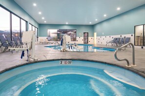 An indoor swimming pool with multiple lanes, lounge chairs, and a lifeguard stand.
