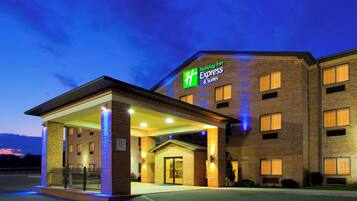 A Holiday Inn Express & Suites building with a brick facade, a covered entrance, and a sign indicating the name and services.