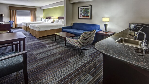 Ein Hotelzimmer mit zwei Betten, einem blauen Sofa, einem kleinen Sessel, einem Schreibtisch und einer Küchenzeile.