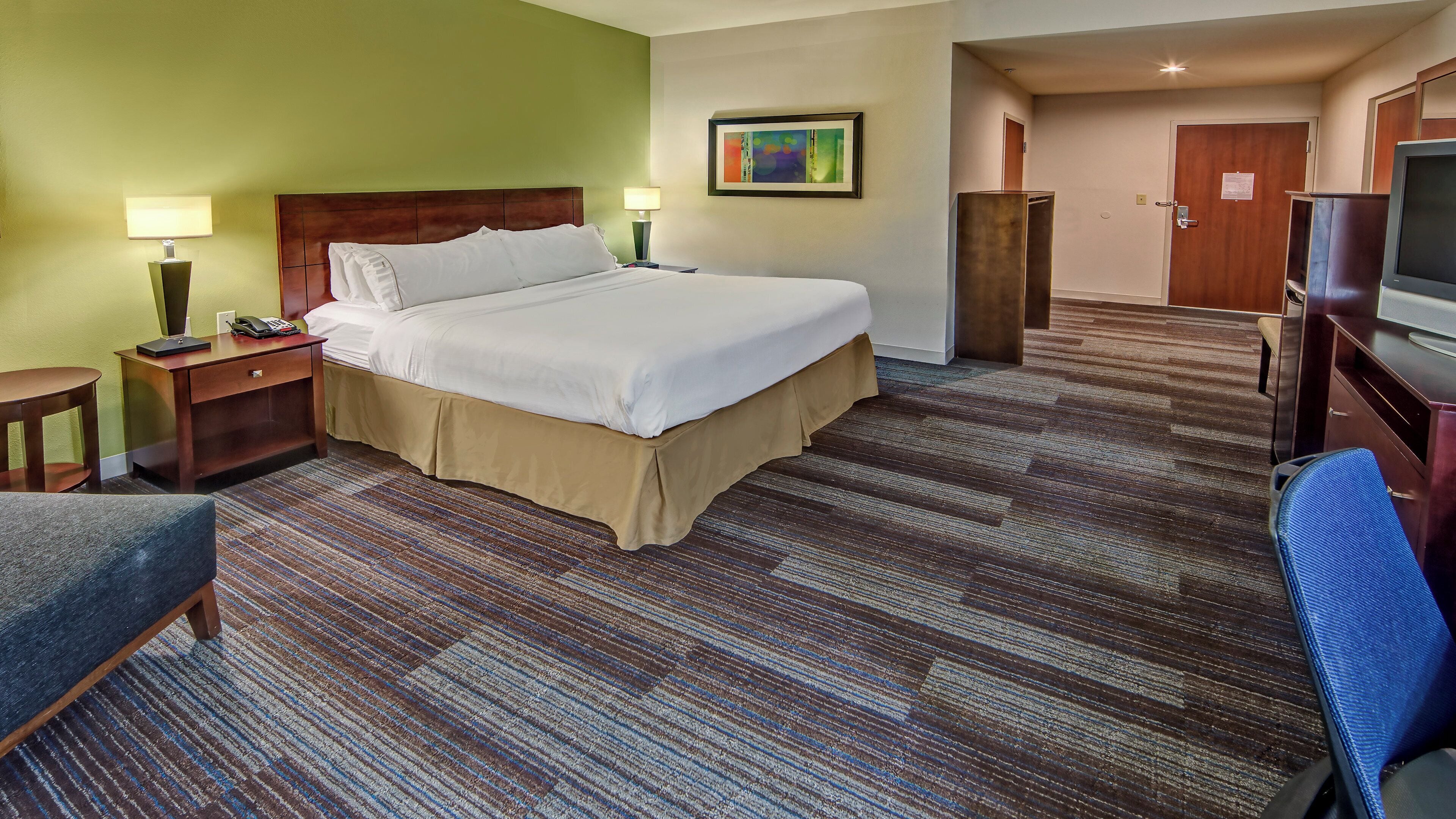 A hotel room with a large bed, a desk, a chair, a TV, and a painting on the wall.