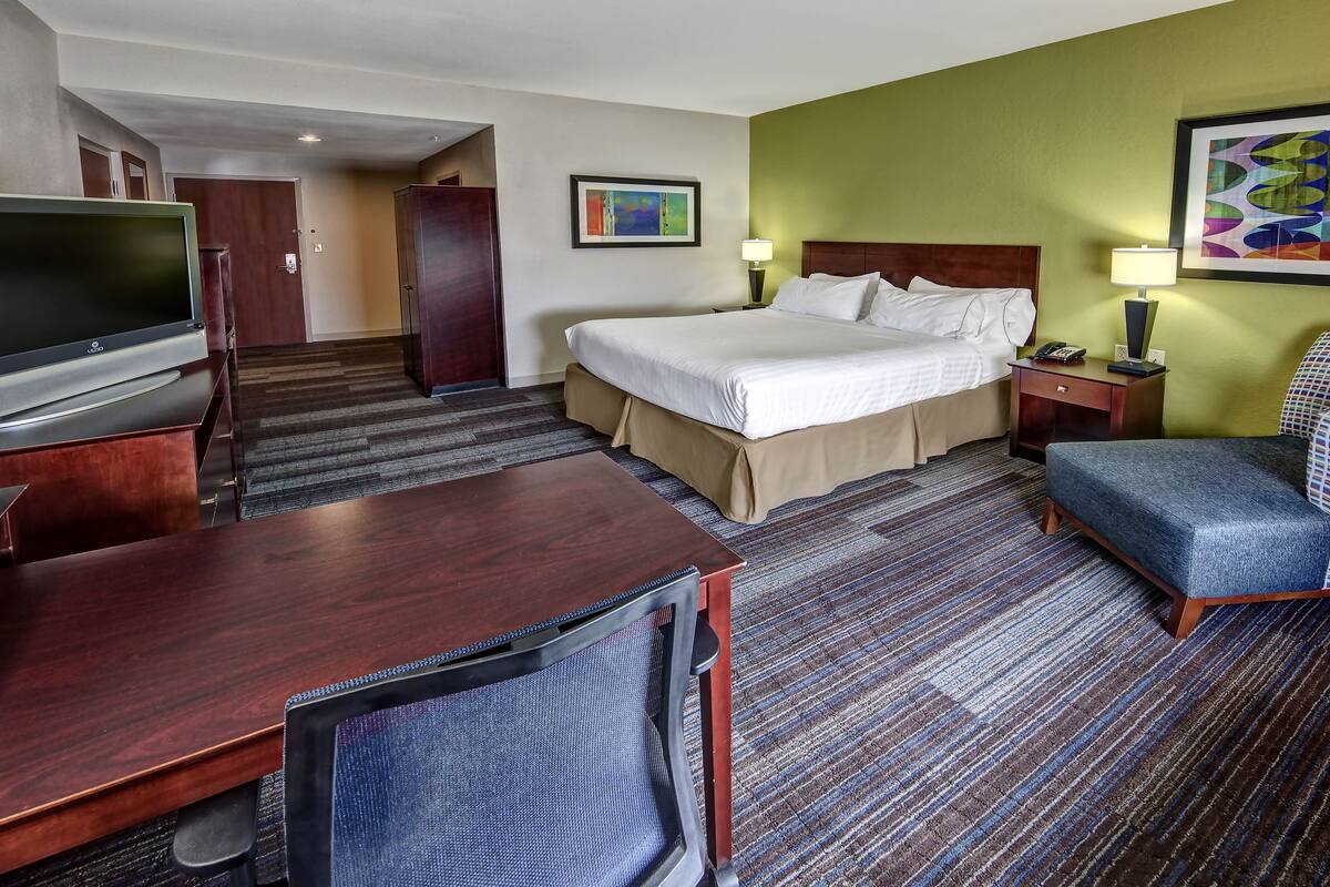 Een hotelkamer met een bed, een bureau, een televisie, een stoel en een tapijtvloer.
