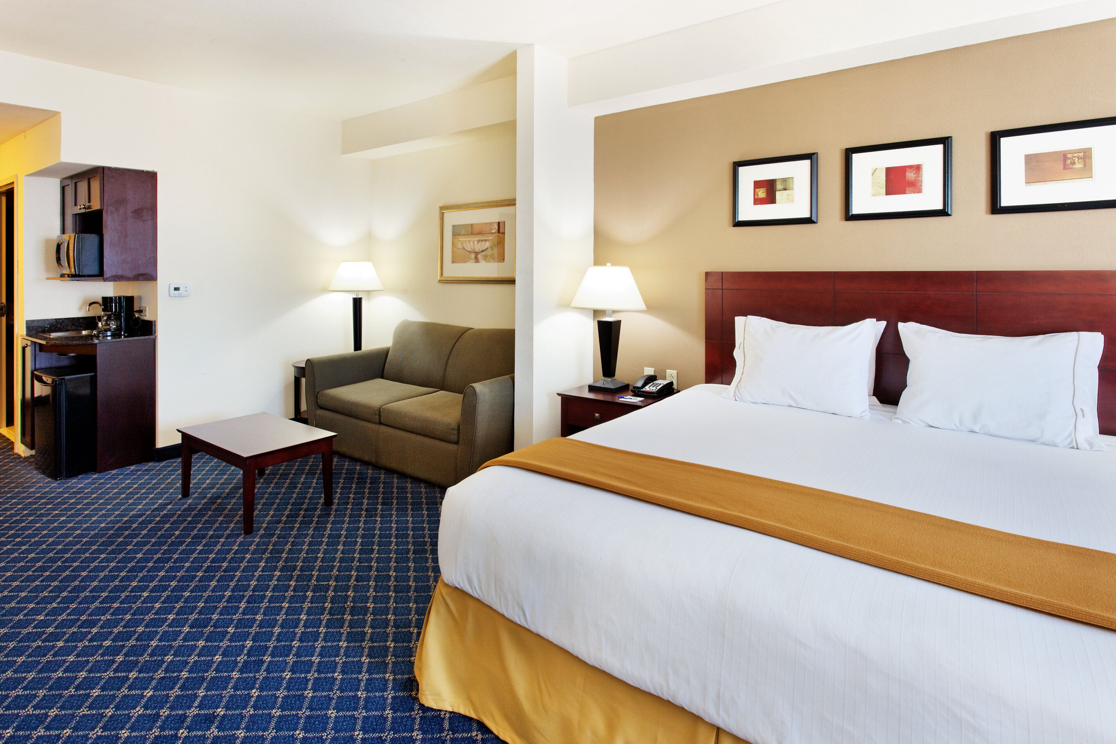 A hotel room with a bed, a chair, a desk, a lamp, and a wall-mounted picture.