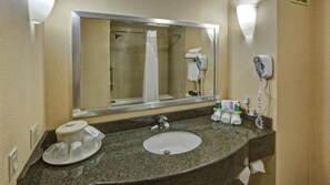 Casa de banho com bancada de granito, lavatório, espelho, secador de cabelo e artigos de higiene pessoal.