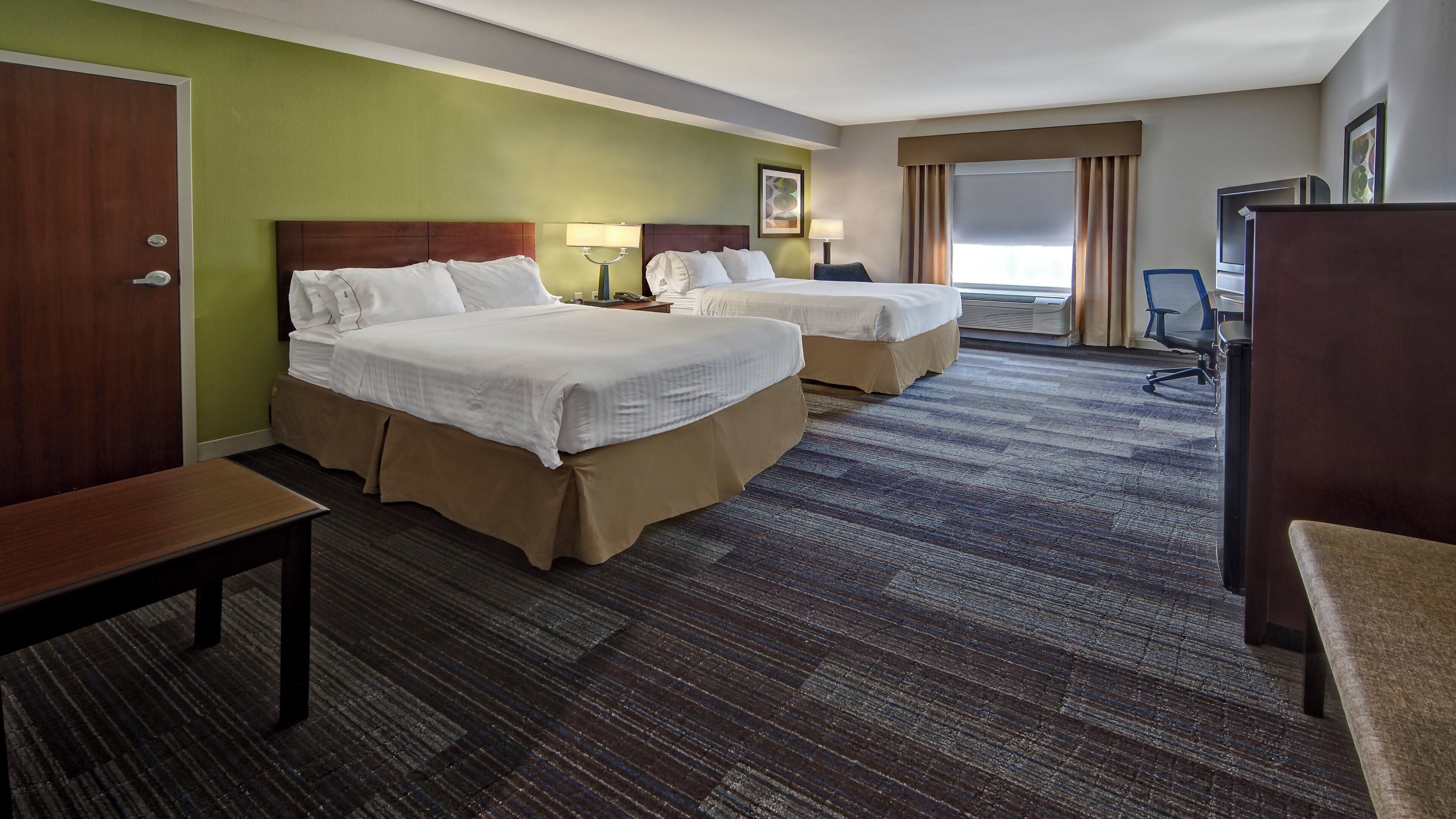 A hotel room with two beds, a desk, a chair, and a large window with curtains.