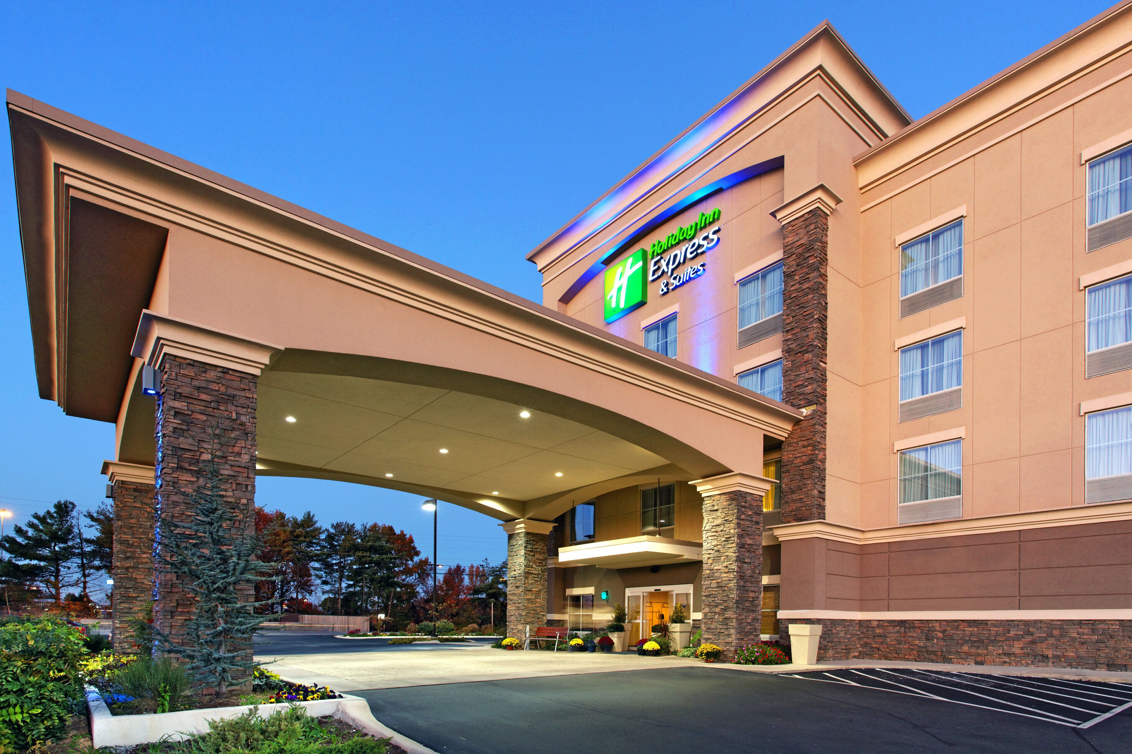 En byggnad som inrymmer ett Holiday Inn Express & Suites-hotell, med en ingång som är skyddad av ett tak och en fasad av tegel.