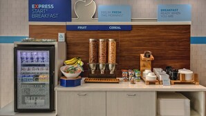 Un espace dédié au petit-déjeuner, comprenant un présentoir réfrigéré, un saladier à fruits, des distributeurs de céréales et divers récipients pour aliments.